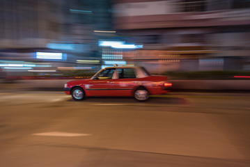 Panning photo of red taxi moving fast on Hong Kong streets