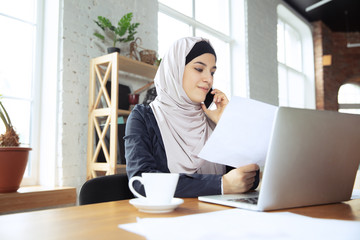 Talking on phone, attented. Beautiful arabian businesswoman wearing hijab while working at openspace or office. Concept of occupation, freedom in business area, leadership, success, modern solution.