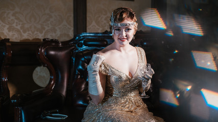 a girl in a gold dress with a diadem on her head, sits on a leather armchair, shows her shoulder...