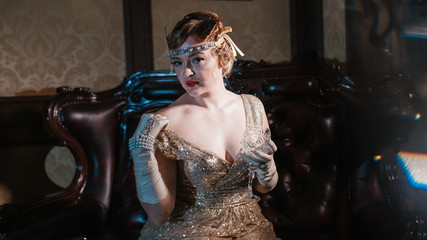 a girl in a gold dress with a diadem on her head, sits on a leather armchair, shows her shoulder...