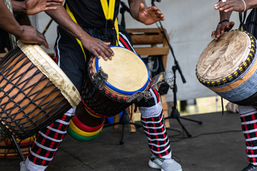 Closeup of three artist performing traditional colorful string wrapped african djembe drums while standing on stage during event