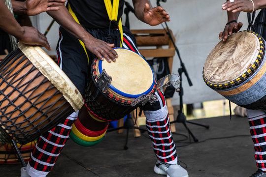 Closeup of three artist performing traditional colorful string wrapped african djembe drums while standing on stage during event