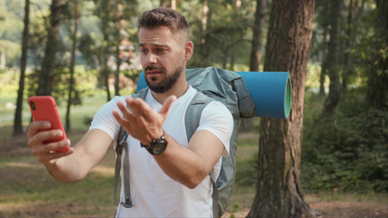 Close up man with beard and backpack in forest uses phone looking for a connection gps application...