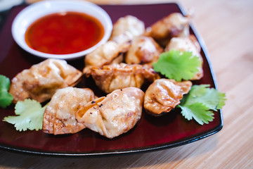 Crispy deep-fried wontons on wooden plate serve with sweet chilli sauce.
