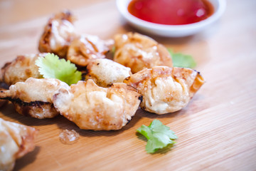 Crispy deep-fried wontons on wooden plate serve with sweet chilli sauce.