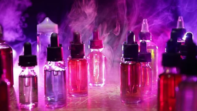 Vape concept. Smoke clouds and vape liquid bottles on dark background. Light effects. Useful as background or vape advertisement or vape background. Selective focus