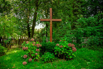 religion cross cemetery grave landscaping view ground hill flower bed vivid green grass cover spring time blooming garden peaceful nature environment on forest edge