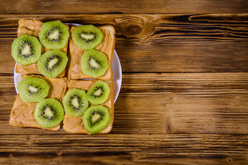 Sandwiches with peanut butter and sliced kiwi fruits in plate on a wooden table. Top view