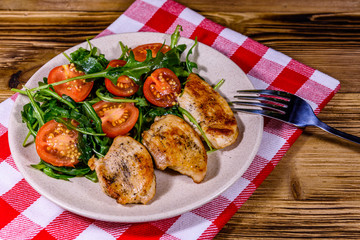 Roasted chicken breasts and salad with arugula and cherry tomatoes in a ceramic plate