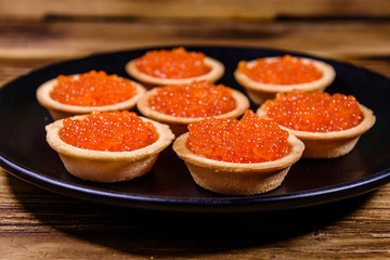 Tartlets with red caviar on a black plate. Festive food