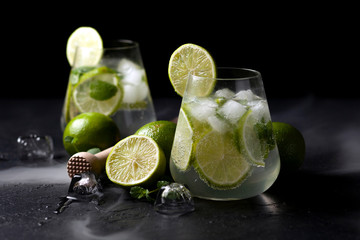two fresh glasses of non-alcoholic mojito, against a dark background, on a black table, summer cocktails with lime and mint