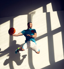 Young athletic basketball player jumping with ball in front of wall with shadows from window