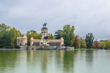 Fototapeta na wymiar monument to King Alfonso XII, featuring a semicircular colonnade and an equestrian statue of the monarch on the top of a tall central core near the lake in Parque del Buen Retiro . Madrid, Spain