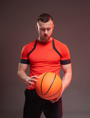 Young athletic man holding basketball ball and looking down on grey background