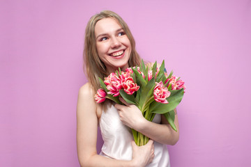 young beautiful girl with a bouquet of flowers on a colored pink background, a woman holds tulips and smiles