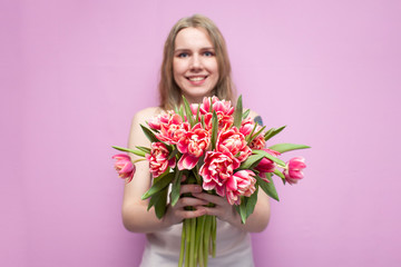 Obraz na płótnie Canvas young beautiful girl holds a bouquet of flowers on a pink background, close-up of a bouquet of tulips