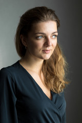 Fototapeta premium Portrait of a young beautiful girl in a room on a background of a gray wall with shadows, natural light from the window.