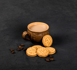 Round shortbread cookies in the shape of coins and a Cup of black coffee with milk on a dark gray background in rustic style