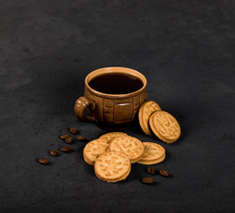 Round shortbread cookies in the shape of coins and a Cup of black coffee on a dark gray background in rustic style
