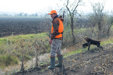A man with a gun in his hands and an orange vest on a pheasant hunt in a wooded area in cloudy...