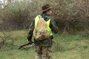 Hunting period, autumn season open. A hunter with a gun in his hands in hunting clothes in the autumn forest in search of a trophy. A man stands with weapons and hunting dogs tracking down the game.