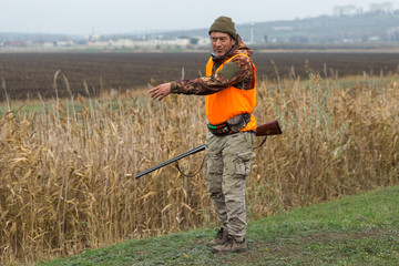A man with a gun in his hands and an orange vest on a pheasant hunt in a wooded area in cloudy...