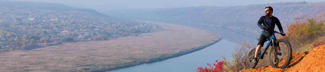 Conquering mountain peaks by cyclist in shorts and jersey on a modern carbon hardtail bike with an air suspension fork . Beautiful view from the mountain. Panoramic view for banner.