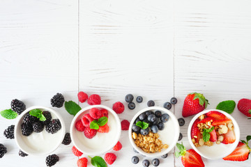 Healthy yogurt bowls with assorted berries and granola. Bottom border against a white wood background. Copy space.
