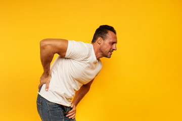Aching man with back pain. Yellow background