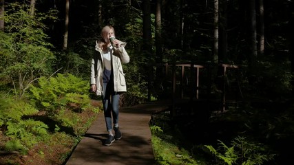 woman walks with a thermomug on a forest trail - Powered by Adobe