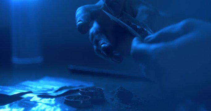 Man rolling a medical marijuana joint in night club. Close up of addict marijuana joint with lighter. Drugs narcotic concept. Close up . Drug use. Man preparing and rolling marijuana cannabis joint.