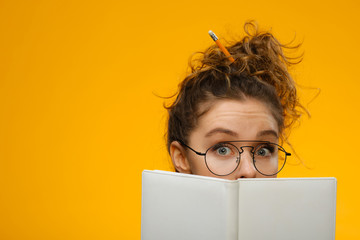 Closeup portrait of teenager hiding behind notebook - obrazy, fototapety, plakaty