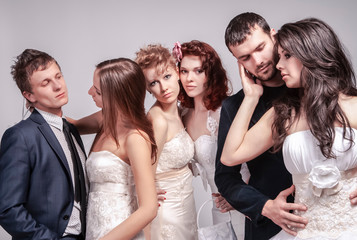 Portrait of Five Loving Caucasian People Posing in Wedding Clothing Together in One Group. Against Gray Background Indoors.