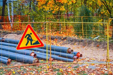 Construction Site Panel in City. Undeground Water Pipes Replacement With Road Sign In Foreground.