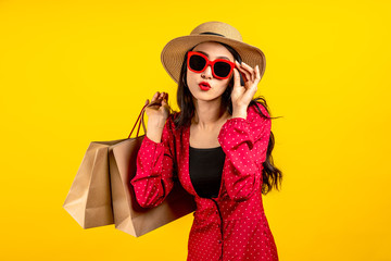 Fototapeta premium Asian trendy shopaholic woman excited about new purchases or sales holding shopping bags and looking to camera over yellow background. Happy beautiful Asian customer carrying shopping bags.