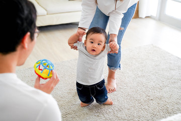 Asian baby boy toddler taking first steps. Family of father and mother encouraging their son...