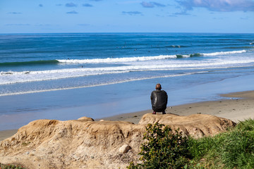 Man squatting on the beach observing a large group of surfers off Mission Beach San Diego