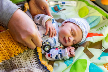 A close up shot on the hands of family doctor checking health of cute baby boy wearing tractor patterned romper suit, listening for healthy heart beat
