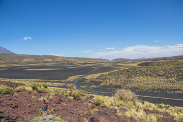 Fototapeta na wymiar Hermoso paisaje volcánico con un camino ondulante. Predominan los colores negro, amarillo, rojizos y el cielo azul