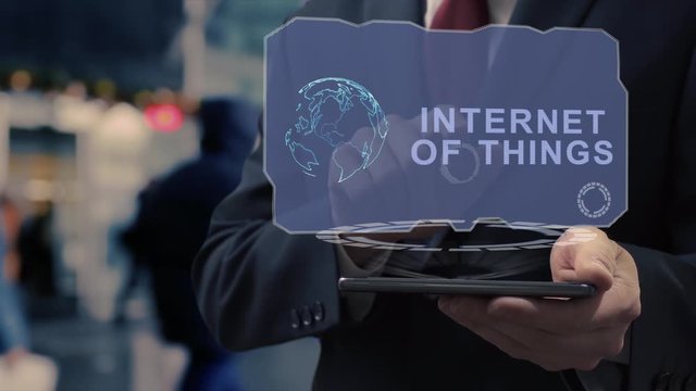Unrecognizable businessman uses hologram on smartphone with text Internet of things. Man in shirt and jacket with holographic screen on background of entrance to the airport or train station