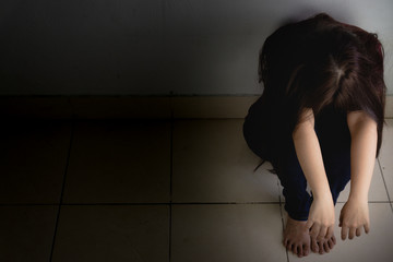 sad woman hug her knee and cry sitting alone in a dark room. Depression, unhappy, stressed and anxiety disorder concept
