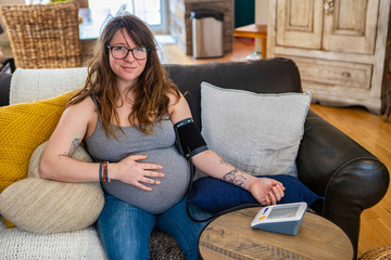 A front portrait of a smiling woman in the third trimester of pregnancy with hand on swollen belly,...