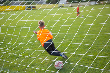 Goalkeeper catches the ball. Goal net in focus. Sports competition. Children's football on the field. Physical development. Children's sport. Sleight of hand. Ball Championship.