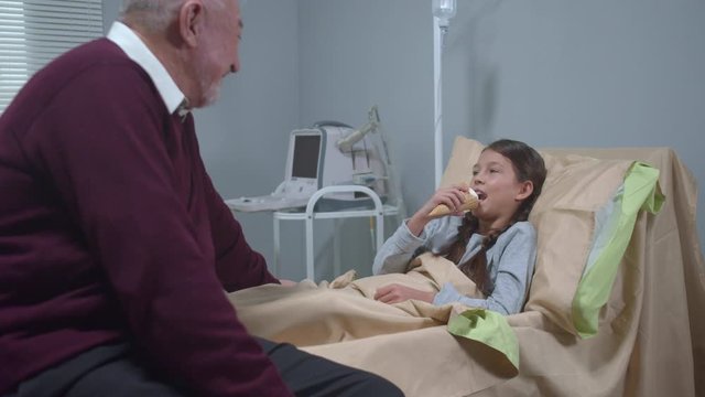 Girl lie on the bed, eat icecream and talk to her grandfather