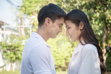 Obraz premium Portrait of beautiful young asian couple in casual dress touching heads with smiling and happy face in green tree background,valentine concept.