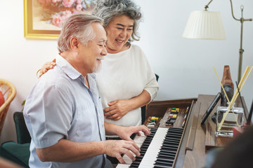 Senior elderly man plays piano in nursing home listened to by elderly woman,Retreatment elderly asian grandmother and grandfather play piano in home with love moment.