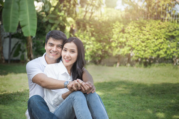 Cute couple have a good time together in front yard,young asian man and woman hug head touch head with happy face and smile with green tree background outdoor with copy space.