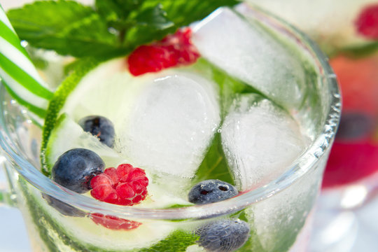 Homemade cold summer cocktail with mineral water, ice cubes, mint, lime, berry juice and fresh berries in glasses with straws, close-up
