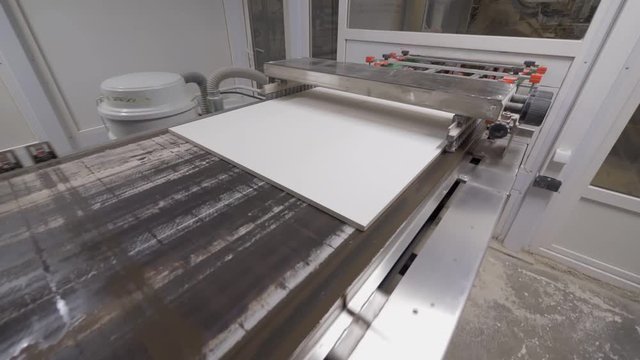painting workshop in factory, ceramic tile is moving on conveyor, machine is applying dye