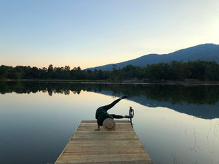 Rear view on young woman sitting on wooden pier in the evening looking at calm lake